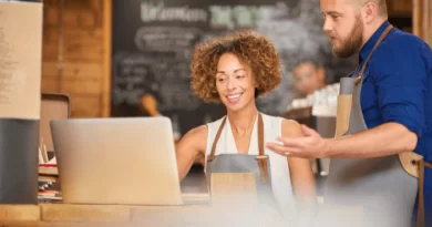 Imagem faz referência à pequenas empresas, em que um casal com avental está em frente a um computador analisando o planejamento financeiro do negócio.